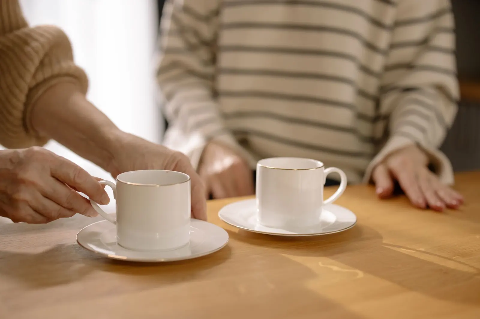 Zwei Kaffeetassen und Hände an einem Holztisch