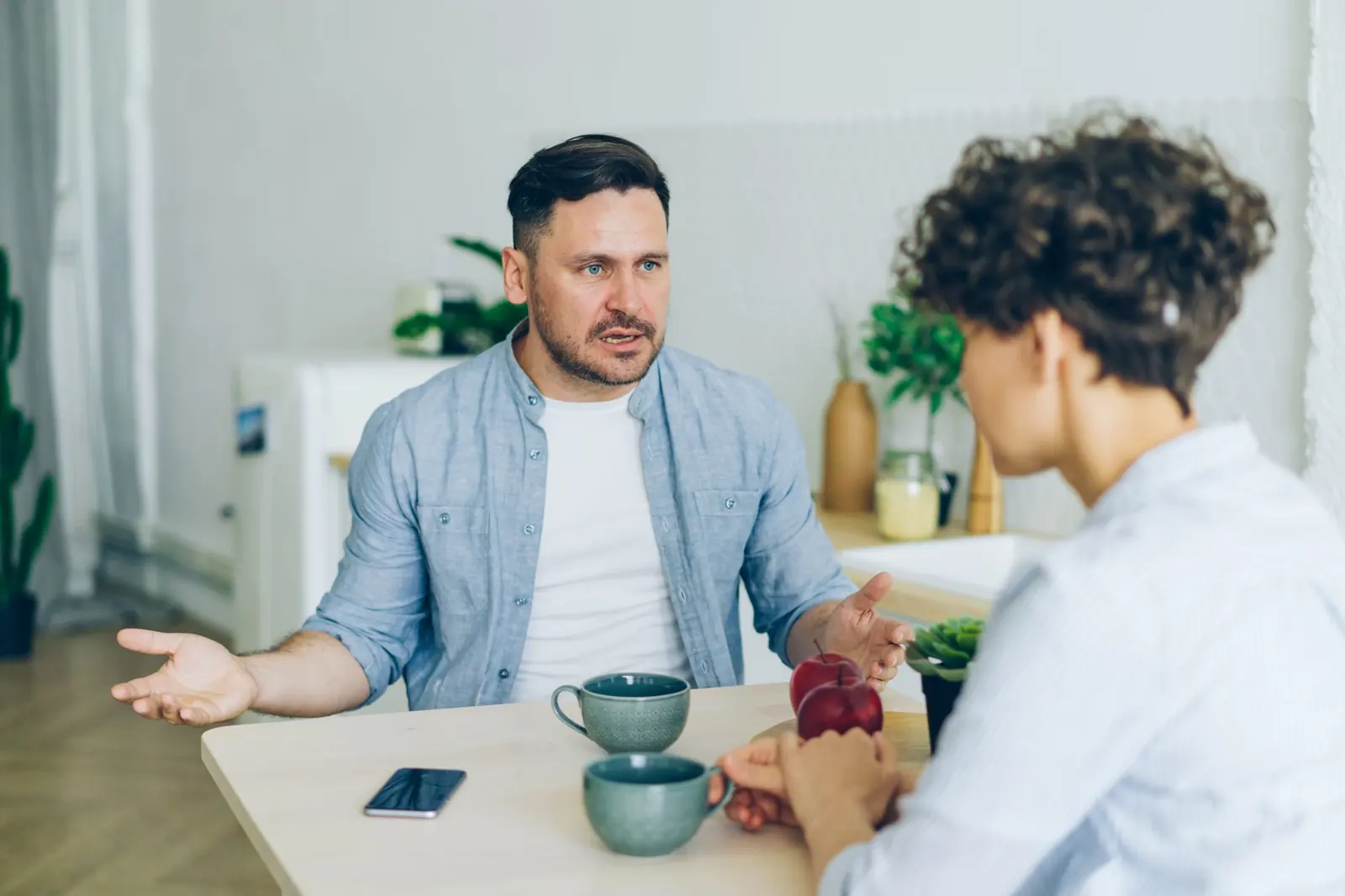 Ein Mann und eine Frau sprechen am Küchentisch miteinander, zwischen ihnen Kaffeetassen